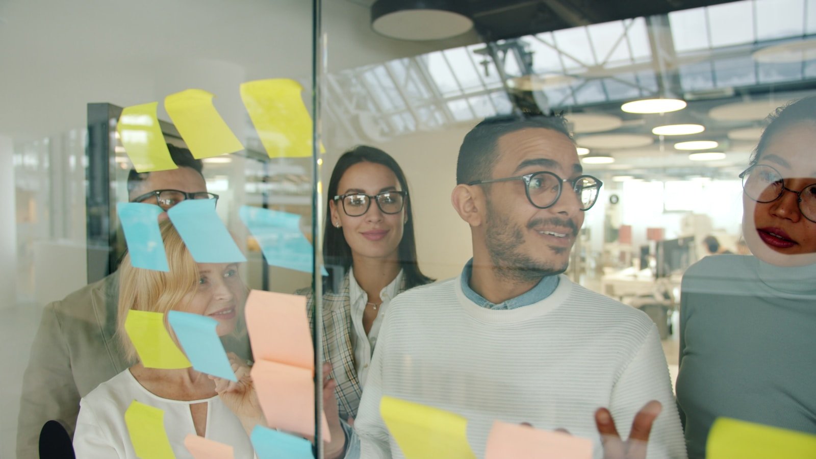 Diverse team brainstorming with sticky notes on glass.