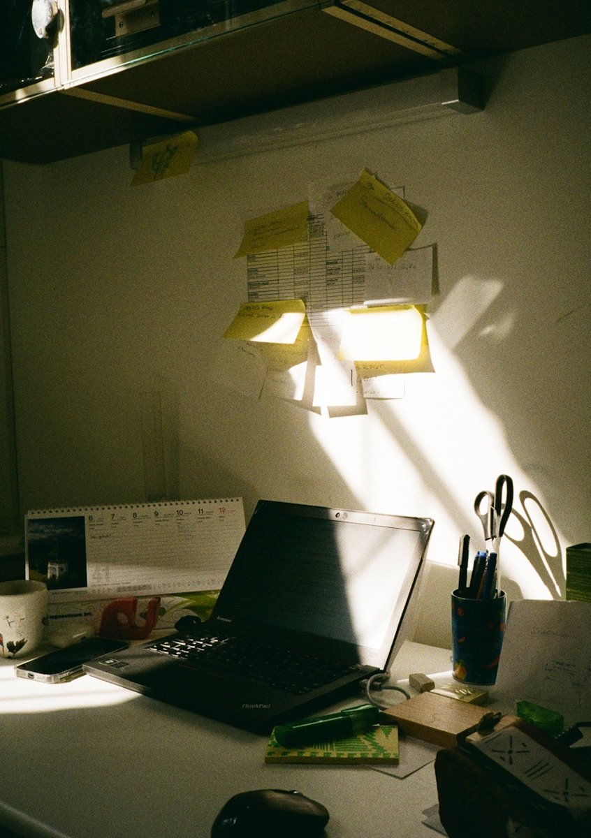 Desk with laptop, sticky notes, and sunlight.